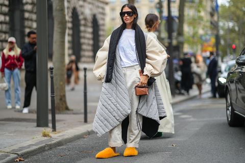 Paris, França 01 de outubro Gilda Ambrosio usa óculos escuros pretos, uma camiseta branca, um lenço preto inchado, uma manga inchada meio bege oversized e metade cinza pálido acolchoado casaco puffer oversized, cintura alta bege calças grandes, anéis prateados, uma bolsa pequena de couro brilhante marrom forma loewe, laranja fofo oversized mules sandálias, fora loewe, durante a semana de moda de Paris moda feminina primavera verão 2022,  Em 01 de outubro de 2021 em Paris, França Photo by Edward Berthelotgetty Images